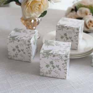 Decorative floral gift boxes on a table with a bouquet in the background.
