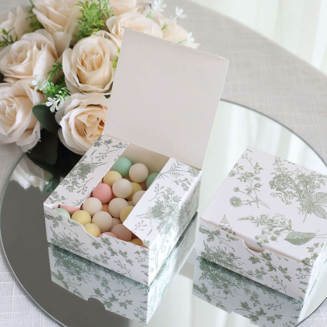 Pastel-colored candy in a decorative floral box on a mirrored surface.