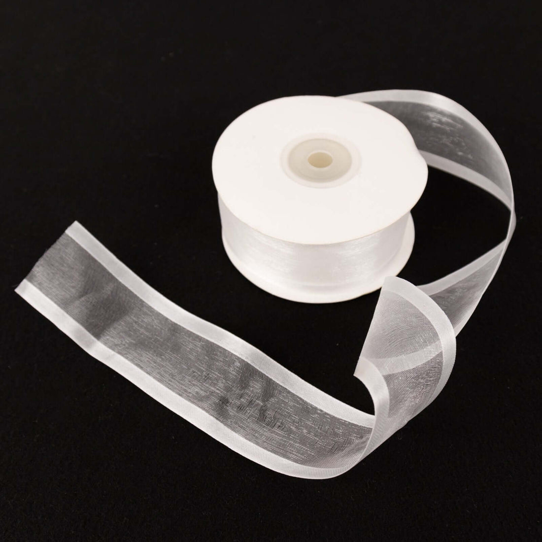 Clear satin ribbon roll with a loose ribbon strand.