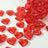 Red heart-shaped glass gems scattered on a white surface.