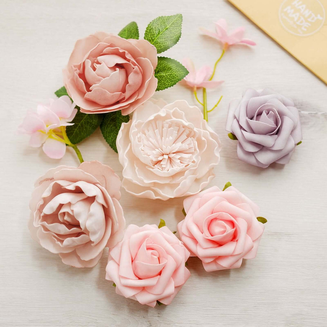 Assorted artificial flowers in pastel colors on a light surface.