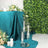 Elegant glass candle holders on a teal table with greenery backdrop.