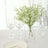 Glass vase with white flowers next to elegant tableware and wine glasses.