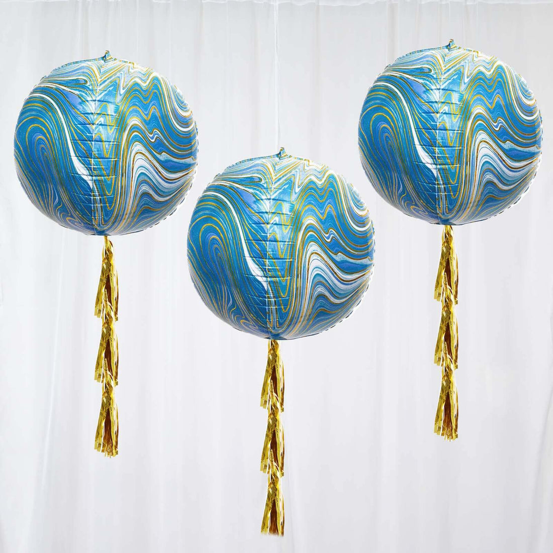 Colorful marbled balloons with gold tassels hanging against a white backdrop