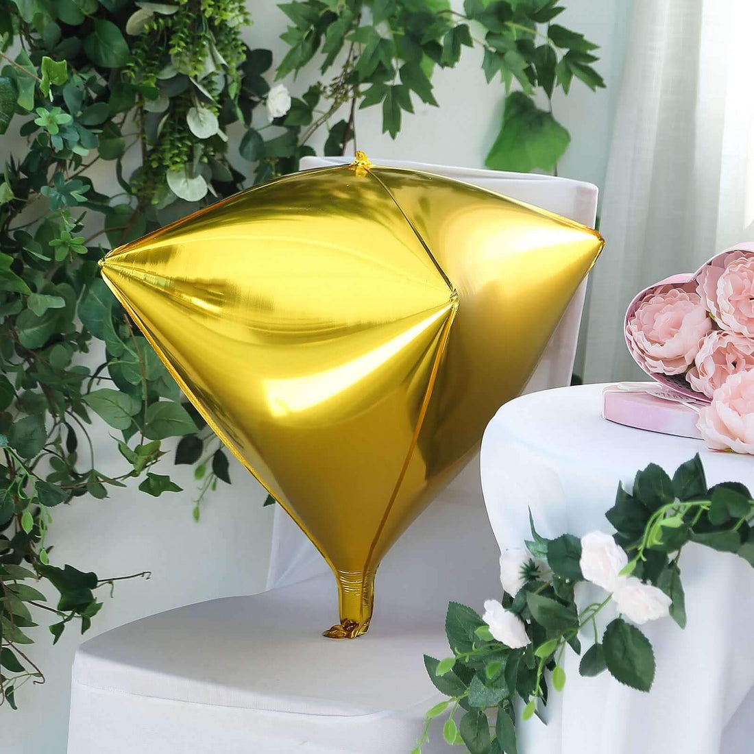 Gold diamond-shaped balloon on a chair surrounded by greenery and flowers.