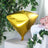 Gold diamond-shaped balloon on a chair surrounded by greenery and flowers.