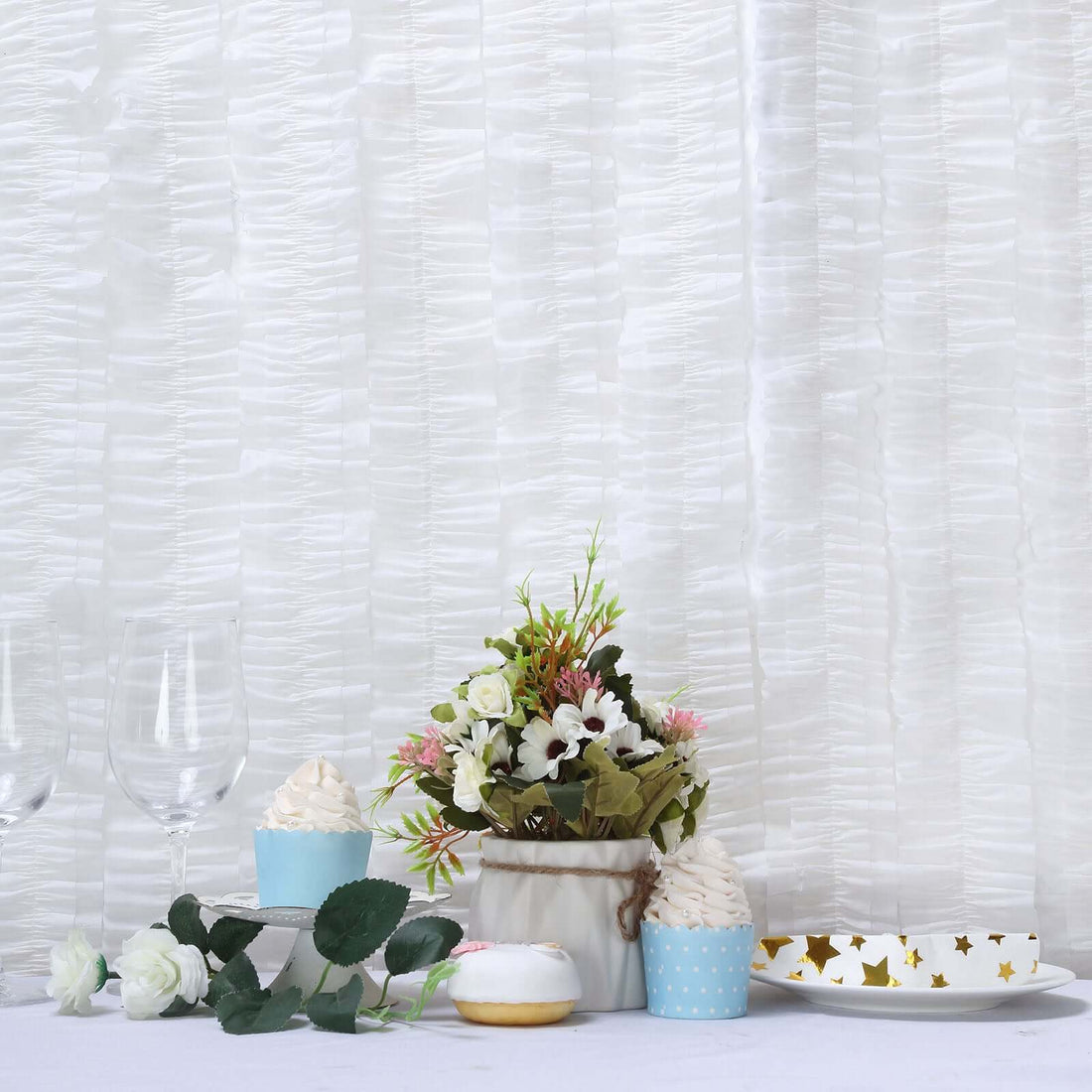 Decorative floral arrangement with cupcakes and tableware on a white table.