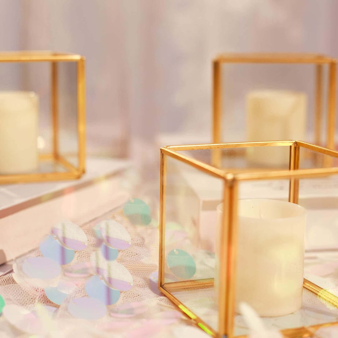 Gold-framed glass candle holders with white candles and colorful confetti.