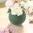 Green vase with flowers on a wooden surface.