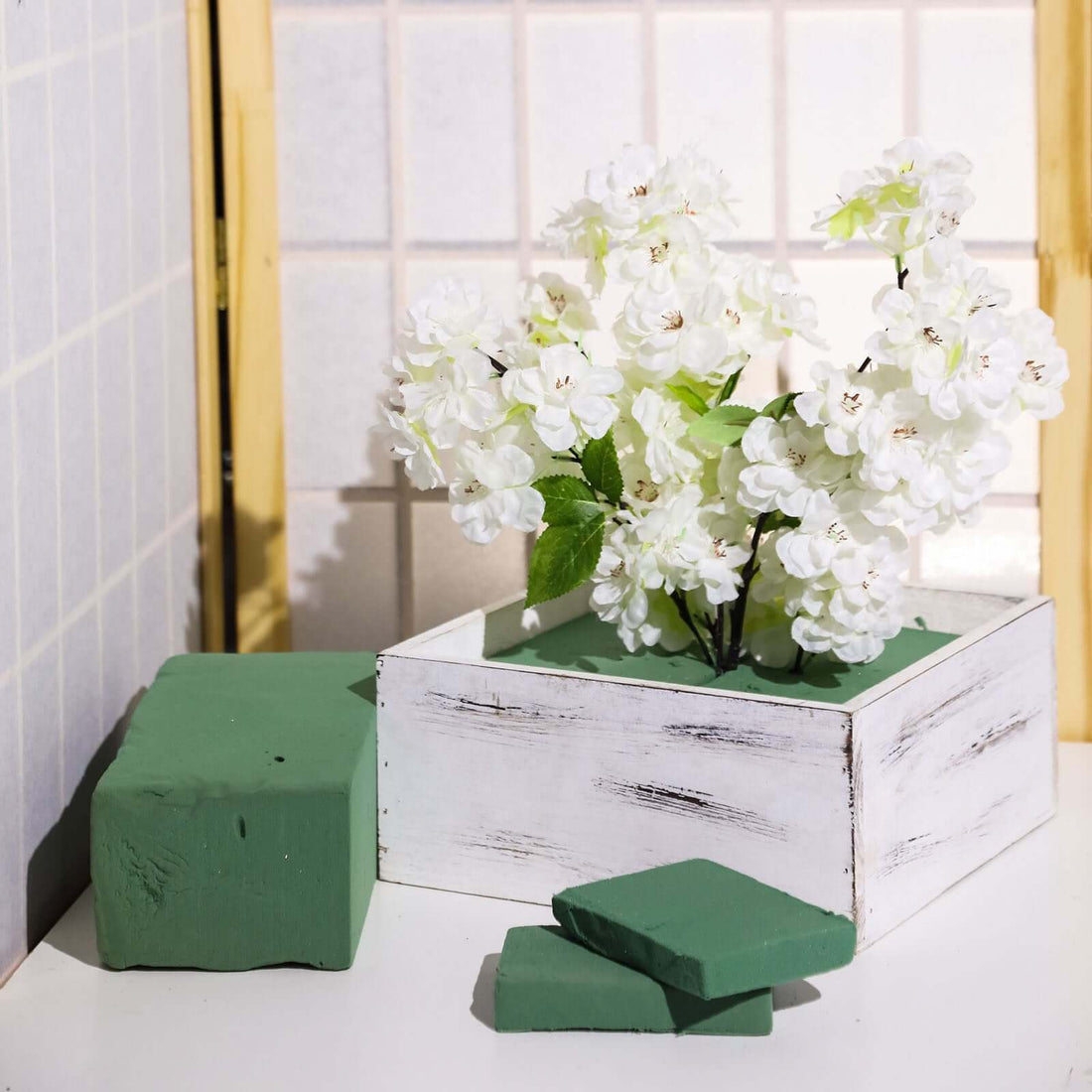 Artificial white flower arrangement in a rustic wooden box with green accents.