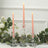 Three elegant glass candlesticks with pink candles and greenery on a table.