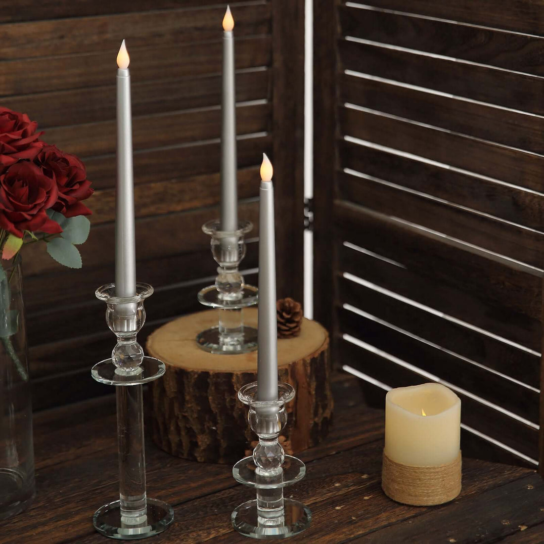 Elegant silver taper candles in glass holders on rustic wooden decor.