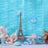 Eiffel Tower figurine with macarons and flowers on a blue background.