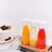 Three glass carafes with colorful drinks on a wooden board beside a cake.