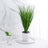 Artificial grass plant in a white pot on a marble tray.