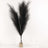 Black pampas grass in a glass vase with two wine glasses beside it.
