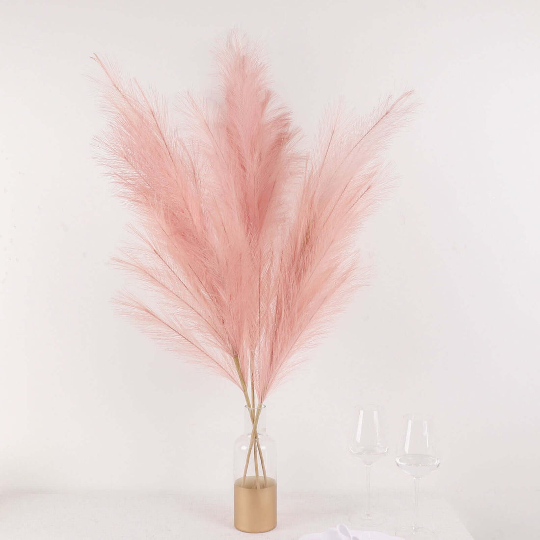Pink pampas grass arrangement in a glass vase with gold base.