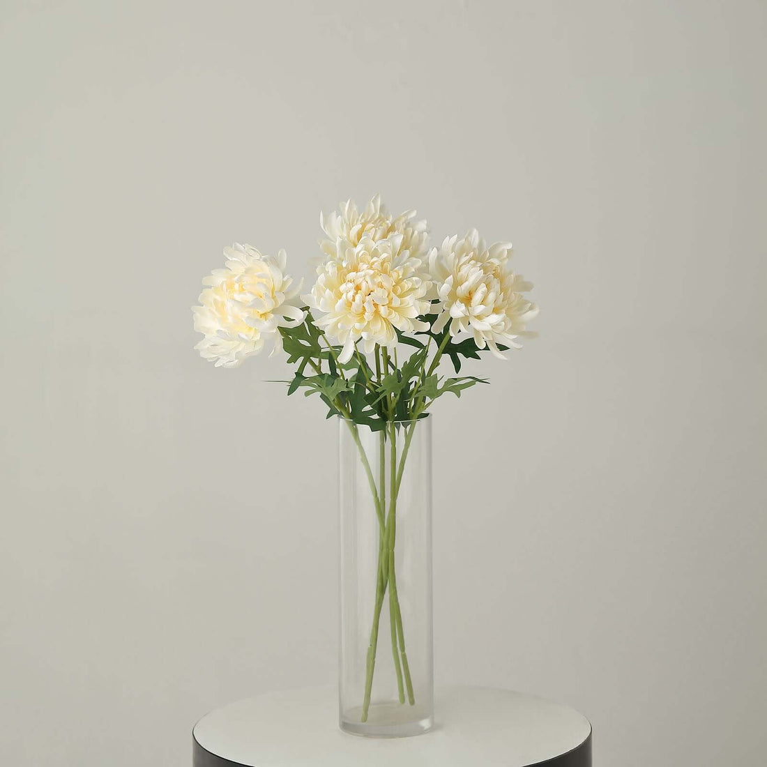 White faux flowers in a clear vase on a round table.