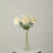 White faux flowers in a clear vase on a round table.