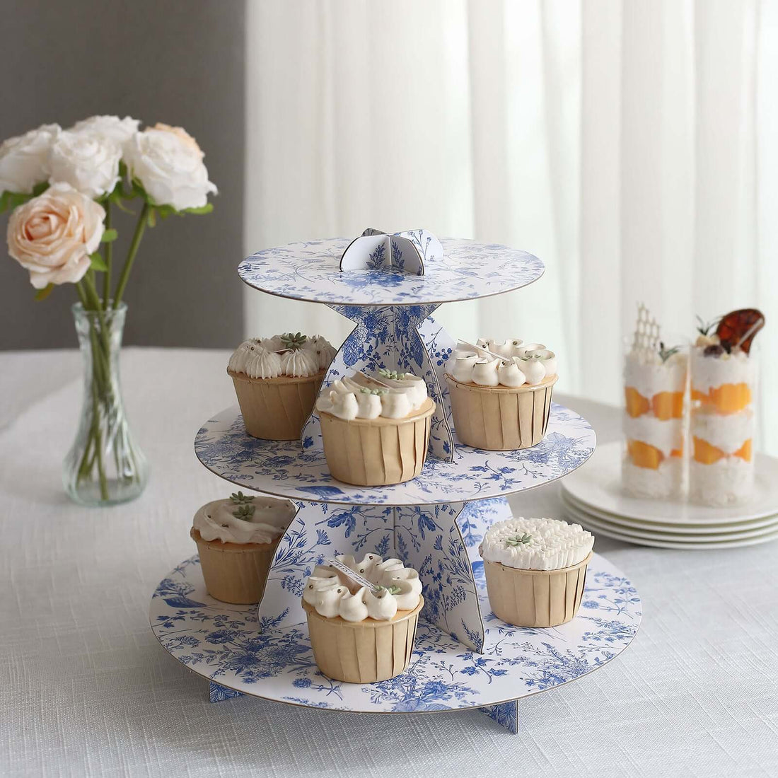 Three-tiered cupcake stand with decorated cupcakes in blue floral design.