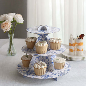 Three-tiered cupcake stand with decorated cupcakes in blue floral design.
