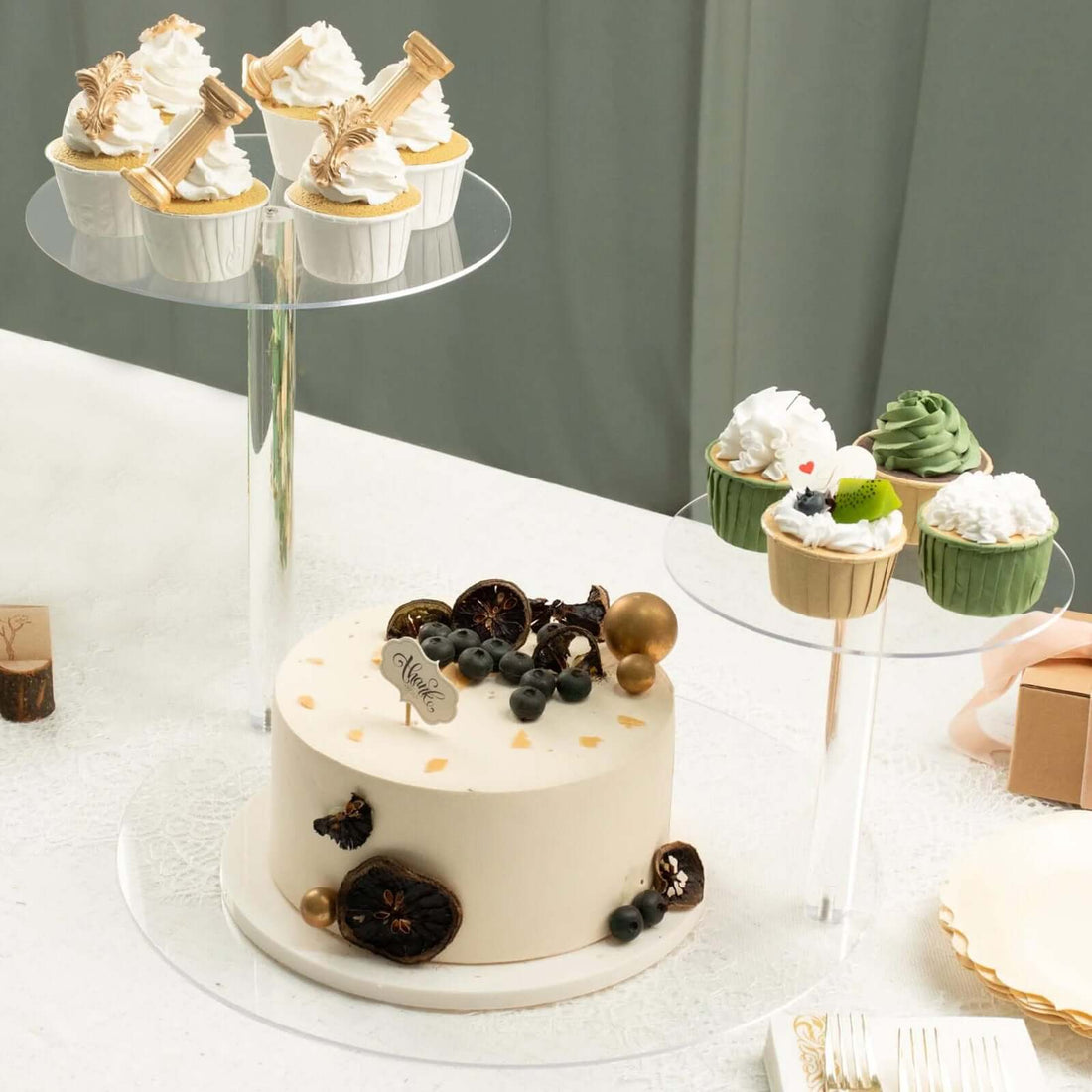 Elegant cake and cupcakes displayed on clear stands at a dessert table.