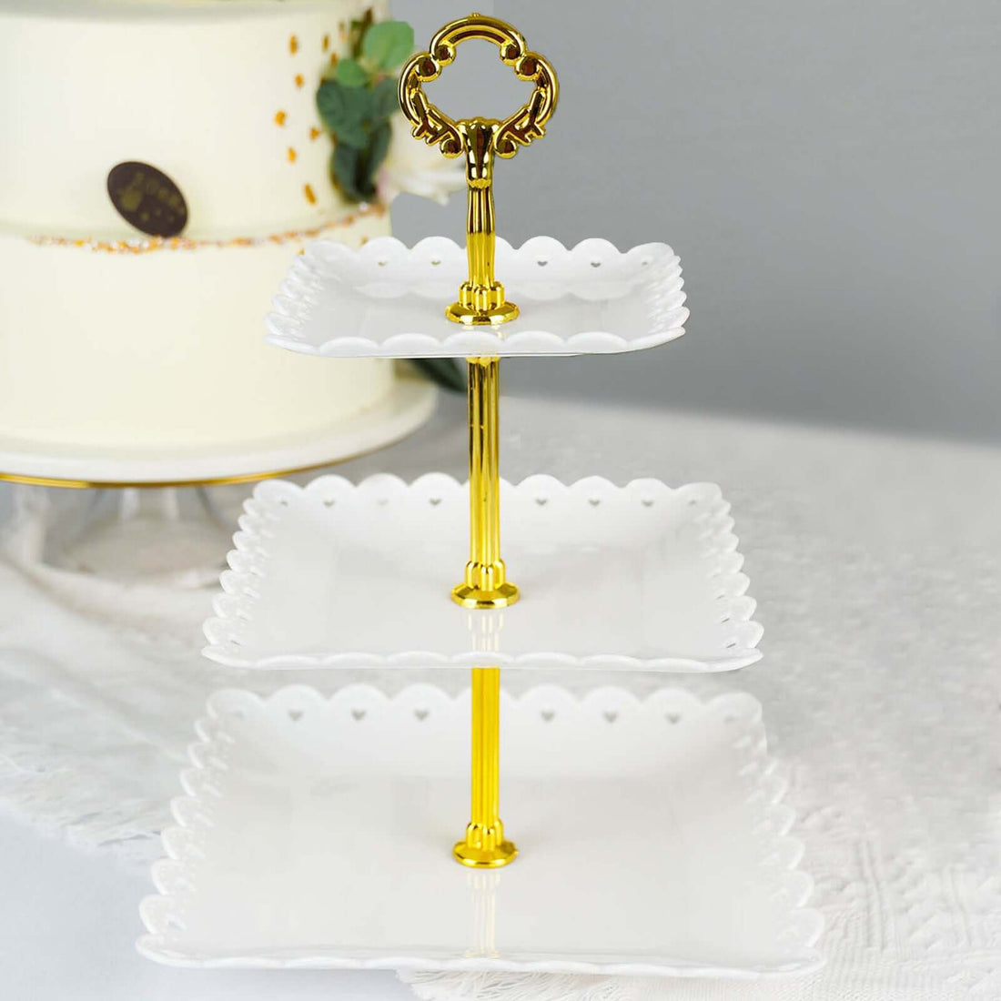 Three-tiered serving stand with a gold handle and scalloped white plates.