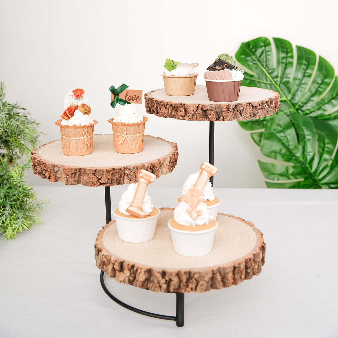 Decorative cupcake display on wooden stands with greenery in the background.