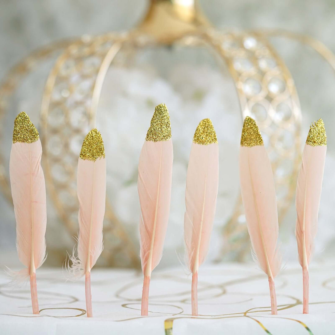 Pink decorative feathers with glittery gold tips arranged in a row.