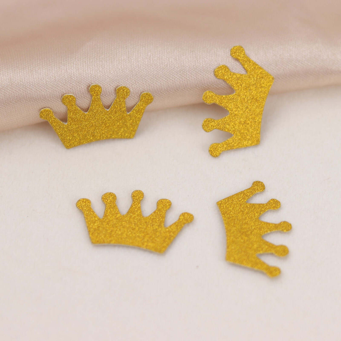 Gold glitter crown embellishments on a soft fabric background.