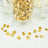 Gold decorative gems in a glass jar with scattered pieces on a soft surface.