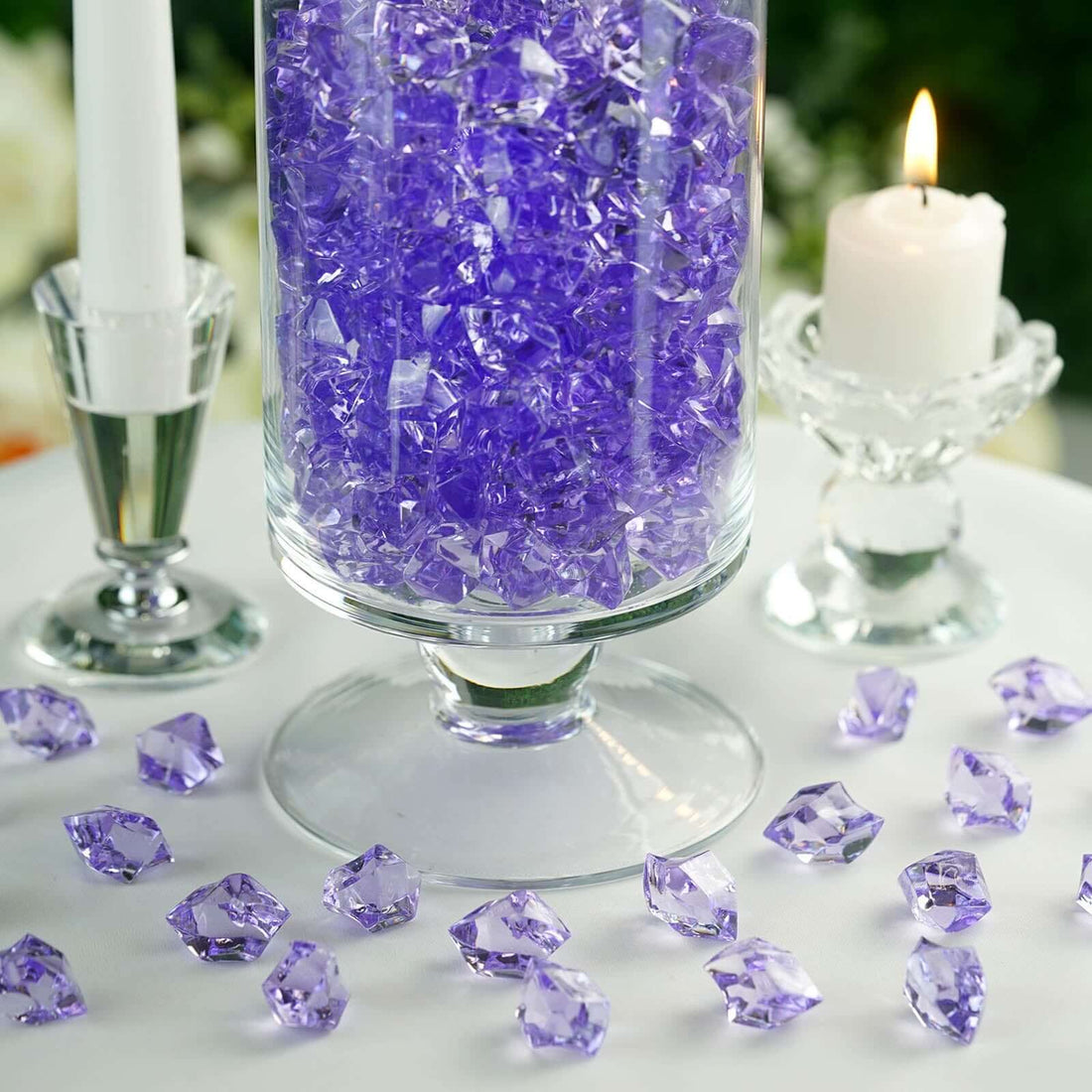 Purple decorative crystals in a glass vase with candles on a table.