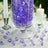 Purple decorative crystals in a glass vase with candles on a table.