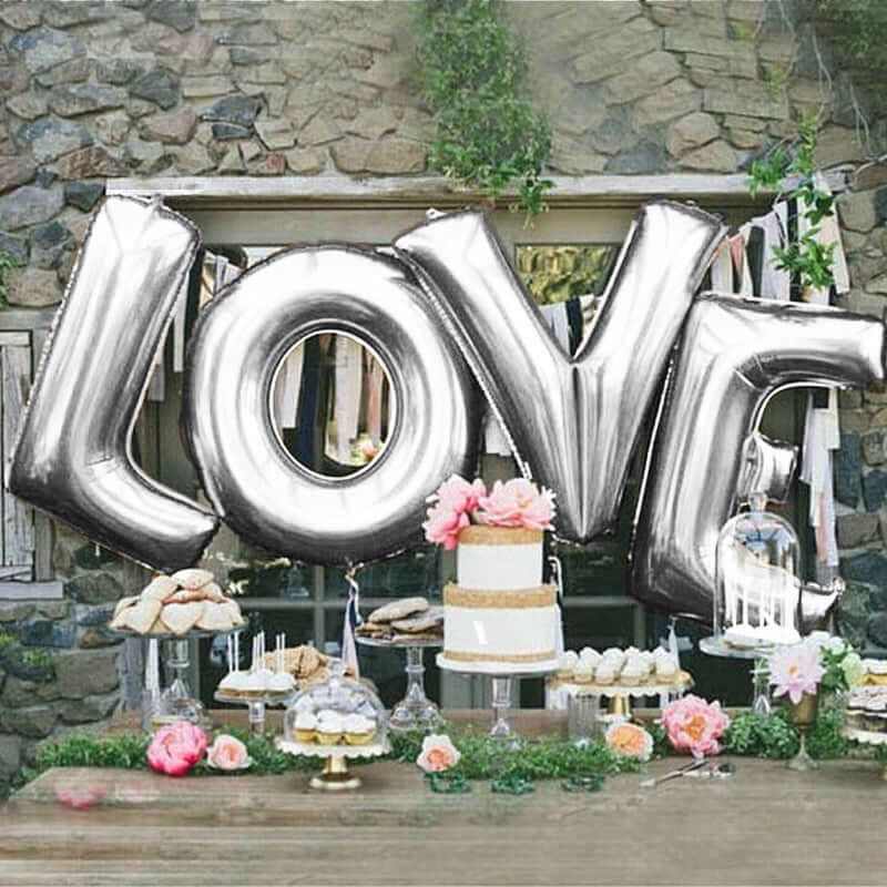 Silver "LOVE" balloons at a wedding dessert table with floral decorations.