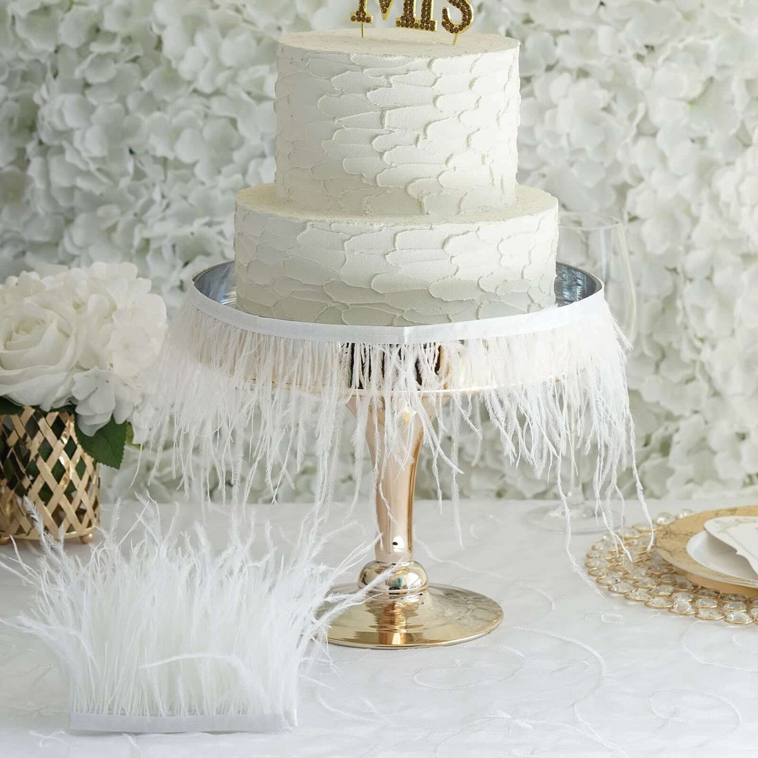 Elegant white wedding cake on a decorative stand with feather trim.