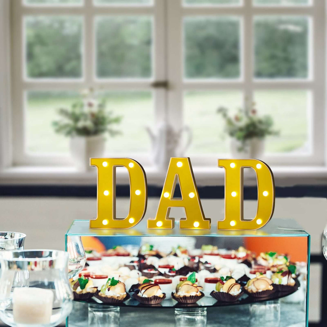 Yellow marquee letters spelling "DAD" displayed above a dessert table.
