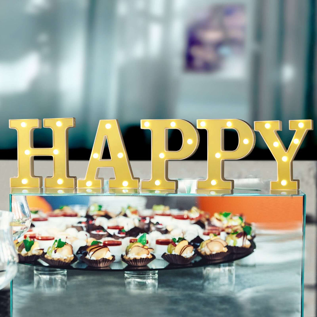 Gold "HAPPY" marquee letters on a table with assorted desserts.