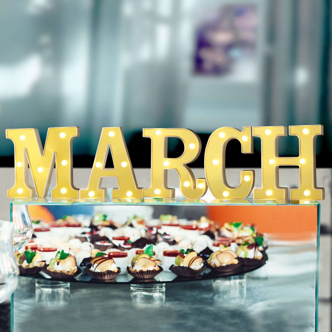 Yellow marquee letters spelling "MARCH" with decorative treats in the background.