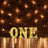 Illuminated marquee letters spelling "ONE" against a brick wall backdrop.