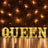 Illuminated marquee letters spelling "QUEEN" against a brick wall backdrop.