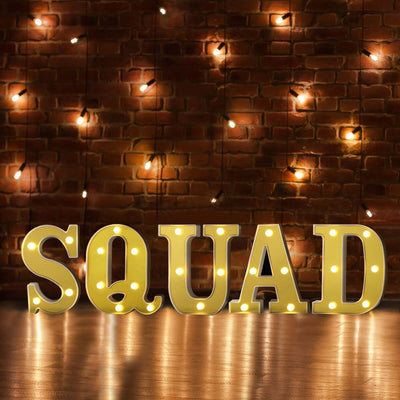 Illuminated SQUAD marquee letters on brick wall with string lights, warm stage backdrop