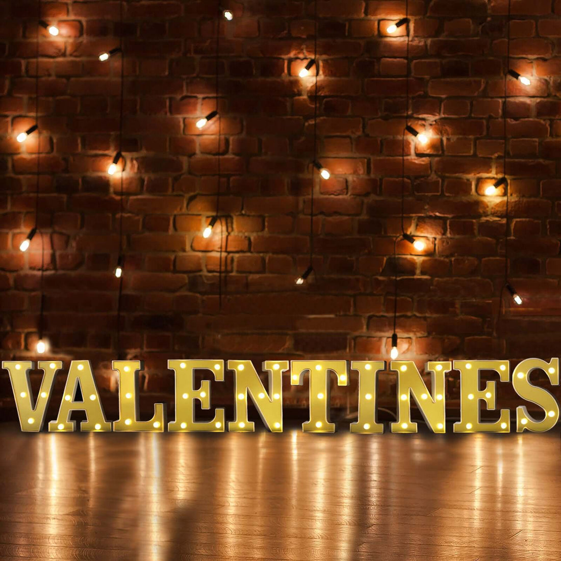 "Illuminated 'VALENTINES' letters against a brick wall with string lights."