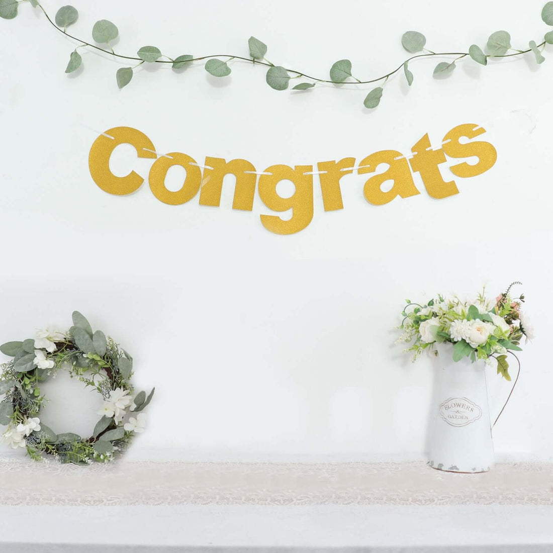 Gold "Congrats" banner with greenery and floral arrangements in a festive setting.