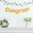 Gold "Congrats" banner with greenery and floral arrangements in a festive setting.