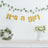 "It's a girl" banner with floral decor and greenery backdrop.