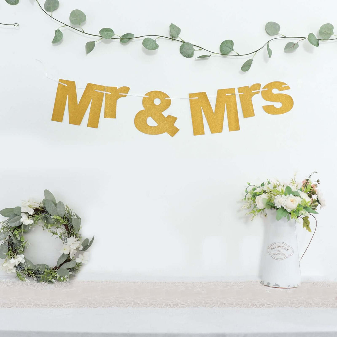 Gold "Mr & Mrs" banner with greenery and floral arrangements.