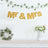 Gold "Mr & Mrs" banner with greenery and floral arrangements.