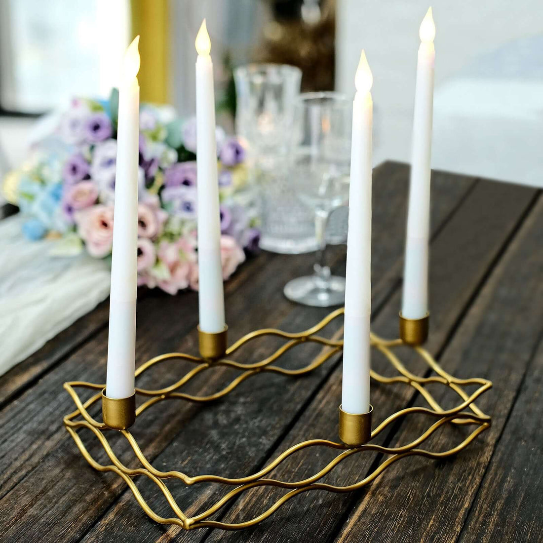Gold candle holder with four white candles on a wooden table.