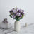 Purple rose bouquet in a minimalist vase on a marble surface.
