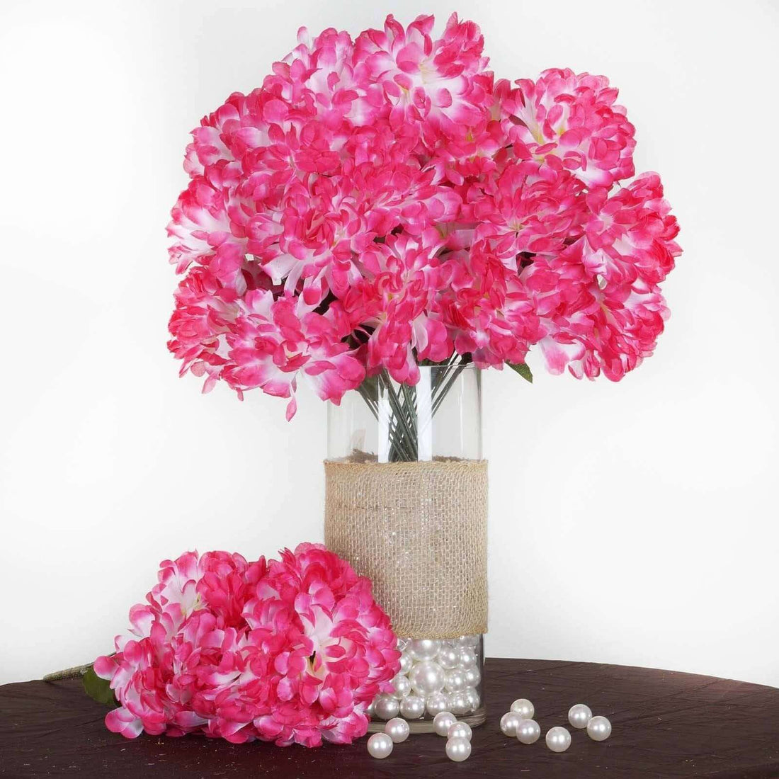Pink artificial flowers in a glass vase with burlap and pearls.